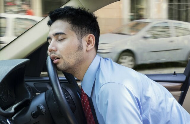 A tired driver yawning while holding the steering wheel, illustrating the dangers of driving fatigued.