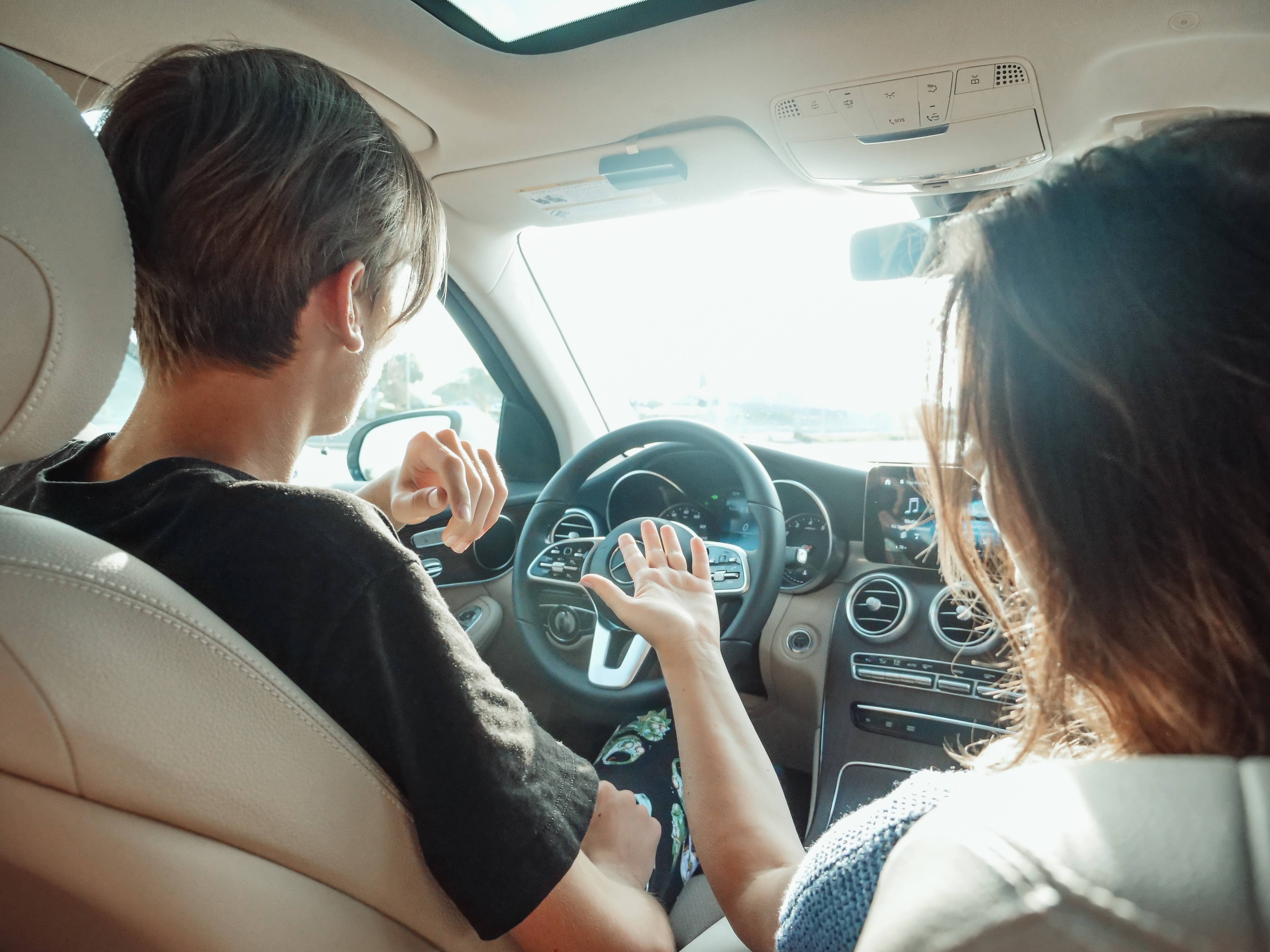 Parent and teenager practicing safe driving techniques in a parked car.