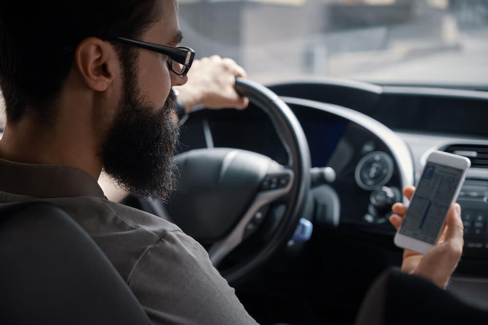 A driver checking their phone while behind the wheel, illustrating the dangers of distracted driving caused by phone addiction.