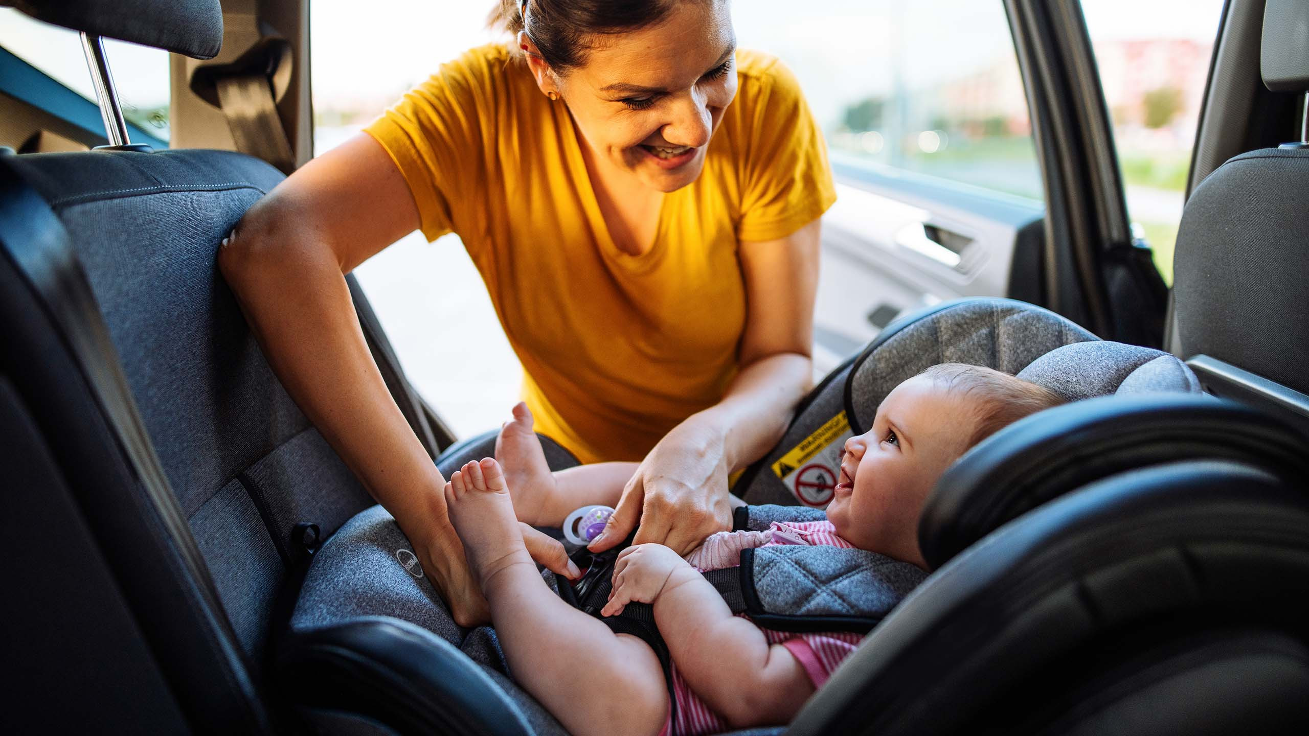 A family preparing for a road trip with their toddler, packing a car and securing a car seat, illustrating essential travel preparations for a smooth journey.