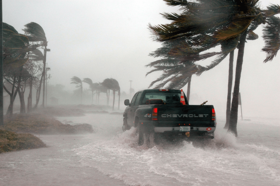 A car driving through heavy rain and strong winds during a hurricane, highlighting the importance of safety tips and precautions for drivers.