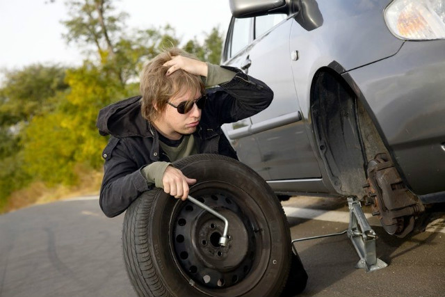 Driver safely changing a flat tire on the side of the road with proper tools and safety measures.