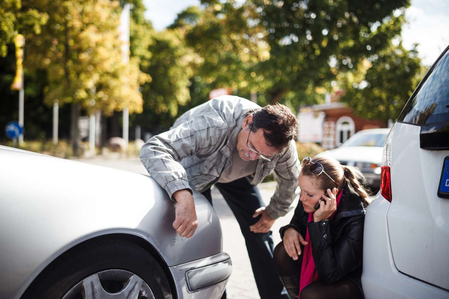 A driver safely documenting a car accident, using their phone to take pictures of the damage while ensuring everyone's safety.