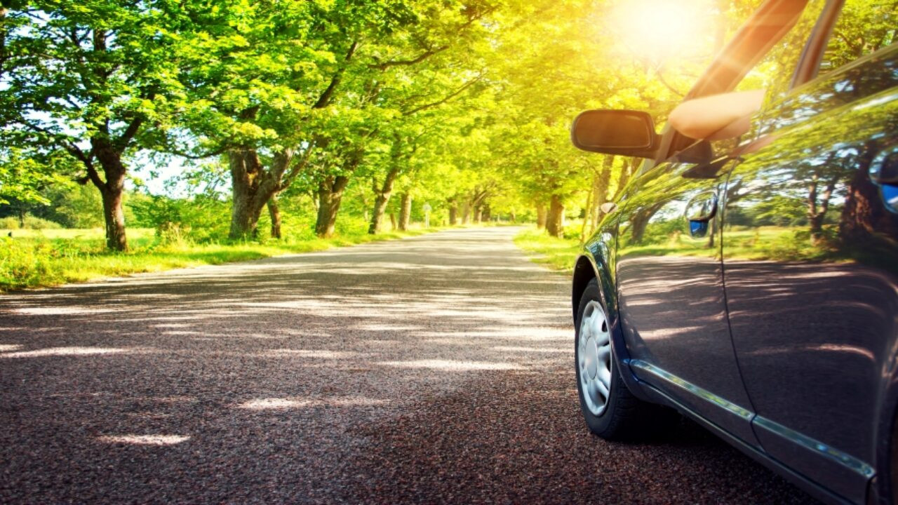 A car driving on a scenic road, surrounded by trees, illustrating eco-friendly driving practices that reduce environmental impact.