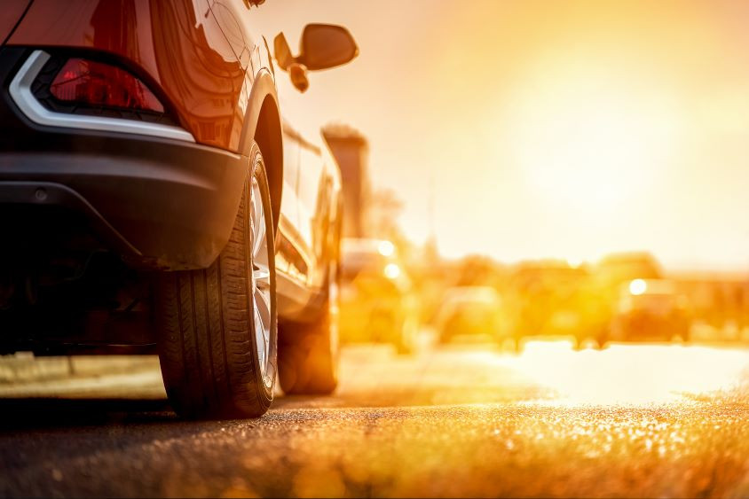 A car driving in the heat of summer, with the sun blazing above, illustrating the effects of high temperatures on vehicle performance.