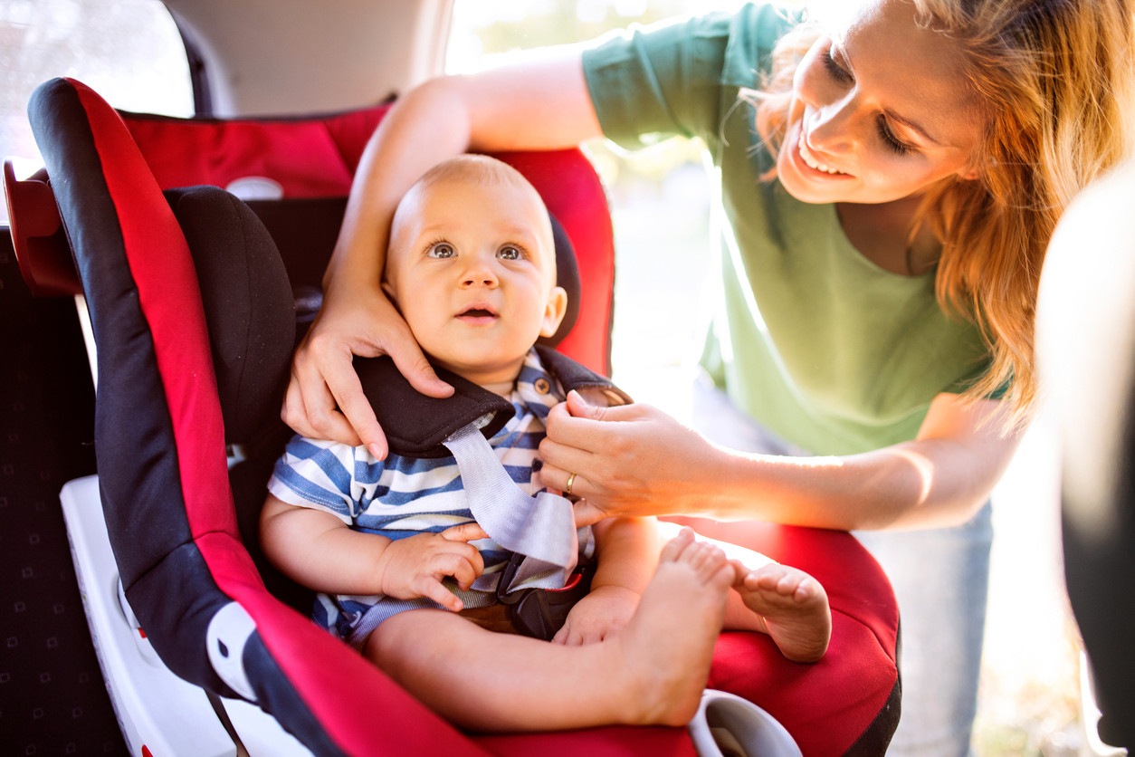 Parent properly installing a child safety seat in the back of a car, ensuring compliance with safety laws as recommended by Get Drivers Ed.