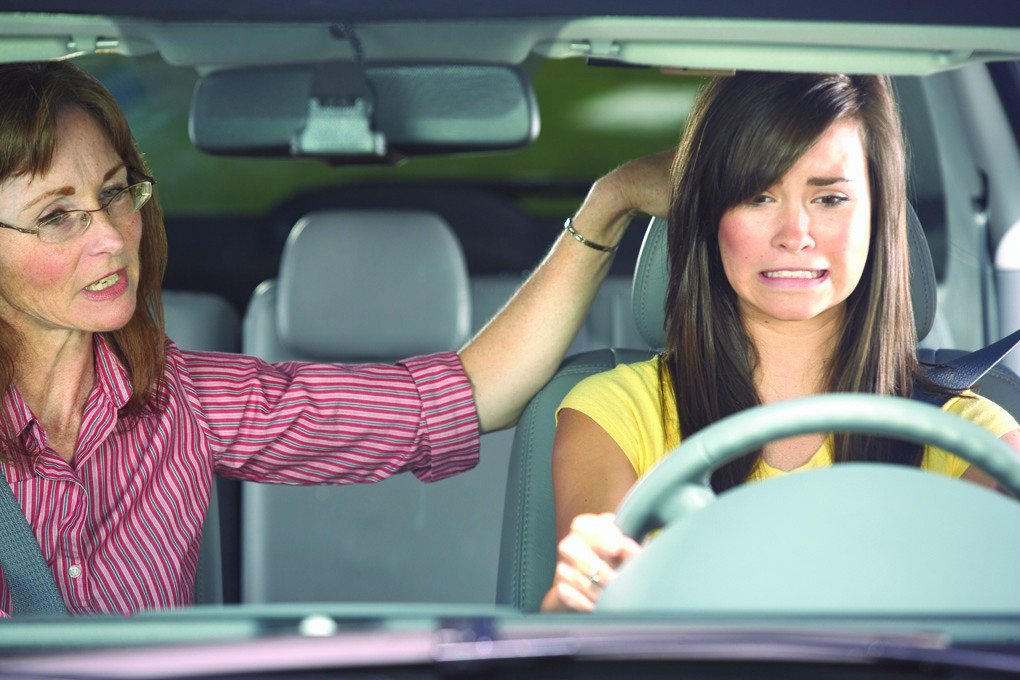 A teen driver confidently holding a steering wheel with a supportive parent guiding them.