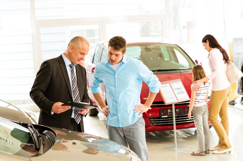 A car dealership showroom with cars and a salesperson, illustrating common dealership tactics buyers should be aware of.