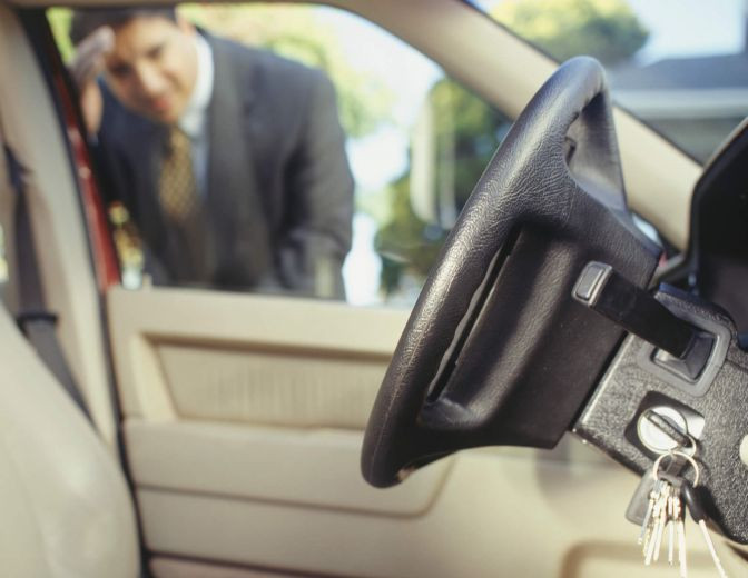 A person standing beside a locked car, looking through the window at their keys on the seat, representing a car lockout situation.