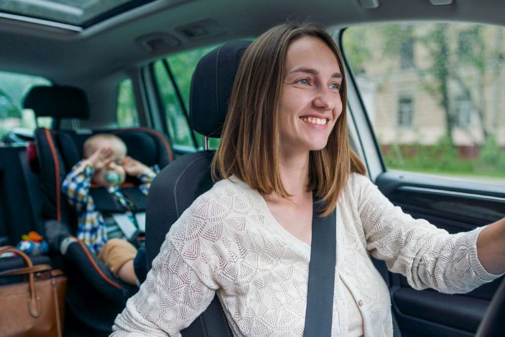 A parent safely driving with a toddler securely fastened in a car seat, focusing on the road ahead.