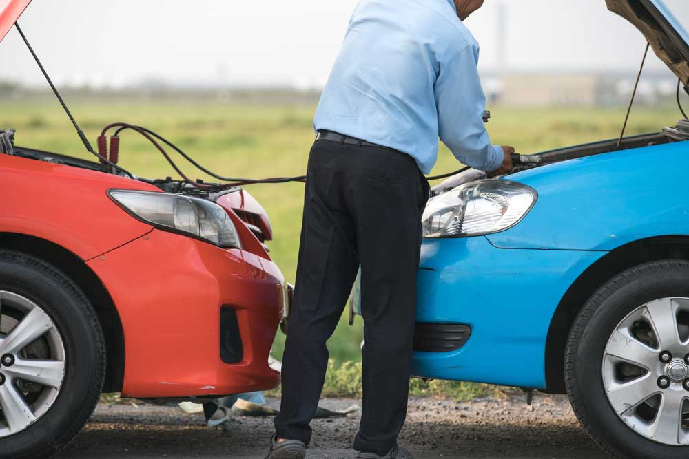 A person safely connecting jumper cables to a car battery, demonstrating the correct way to jump-start a vehicle.